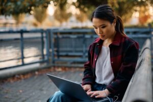 Young woman surfing the net on laptop in the park.