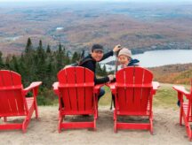 woman and son sitting on red chairs and posing for photos at Mont Tremblant summit. Quebec. Canada.