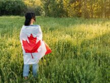 A woman in a field, with a Canadian flag wrapped around them.