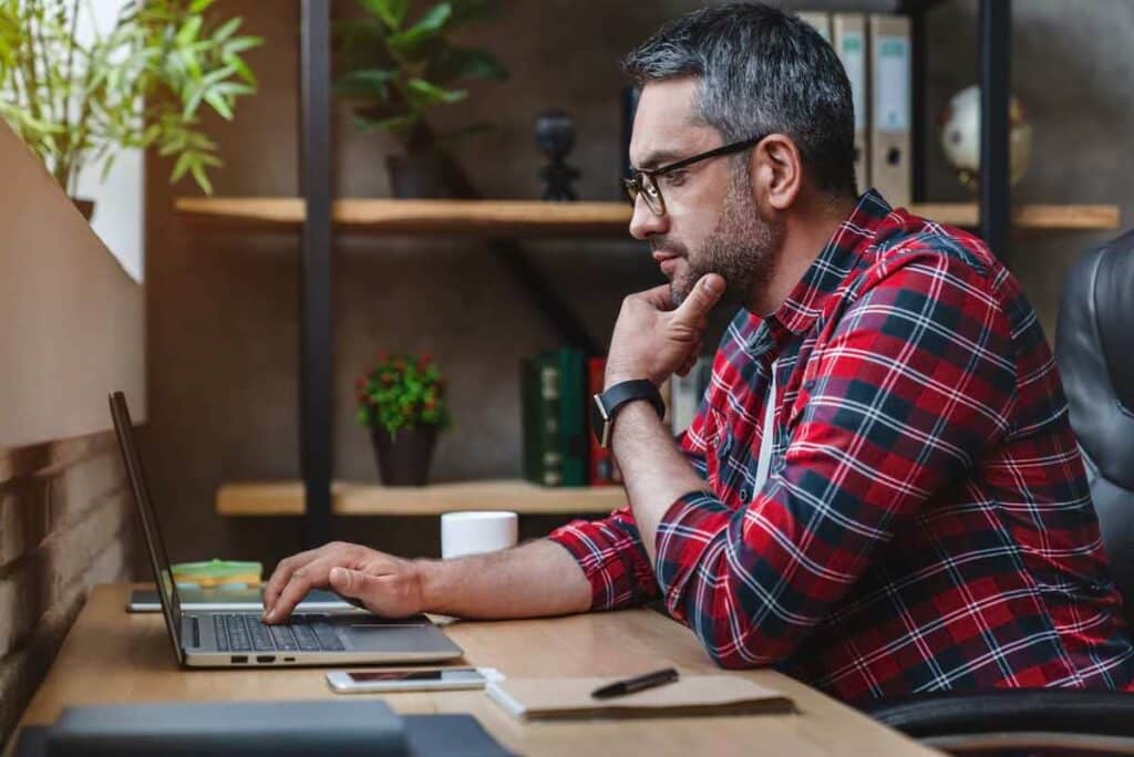 A man looking seriously at a laptop while thinking about something.