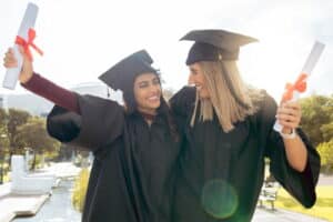 Two friends smiling and celebrating their graduation wearing caps and gowns.