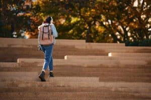 A college student walking on campus steps outside.