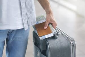 A man's hand holding a passport, a map and a suitcase.