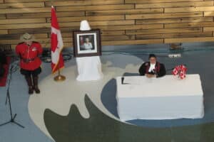 A citizenship judge presiding over a citizenship Ceremony (located in Toronto), with a portrait of Queen Elizabeth II, a Canadian flag, and a Royal Canadian mounted Police officer behind her.