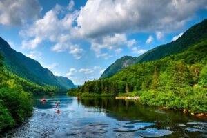 A group of kayakers row down a wide river on a beautiful summer day, with mountains in the background.
