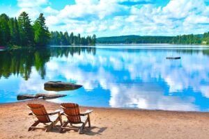 Two beach chairs at the shore of a lake, on a bright summer day.