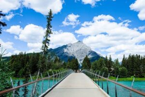 A bridge going over a river in the Banff National Park in Alberta, with mountains and trees visible in the distance.