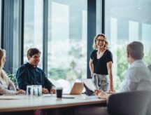 Five coworkers sitting around a large table laughing and discussing work matters.