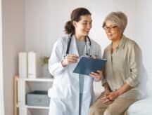 Female doctor talking to a female patient in as she sits on an examination table.