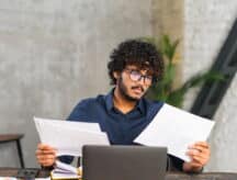 Young man reading papers in front of the laptop