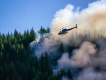 A helicopter carries fire retardant and water over a raging forest fire in British Columbia