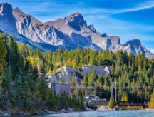A mountain range in Alberta, with a hydroelectric plant visible along the water.