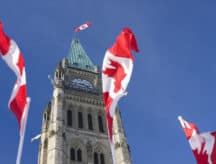 A Canadian flag blowing in the wind before Canada's parliament building.