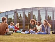A group of students sit on the lawn of their university campus discussing open study permits.