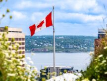 A shot of the coastline and several tall buildings in Halifax, Nova Scotia, with the Canadian flag waving in the centre.