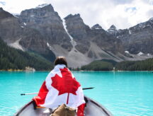 A girl wrapped in a Canadian flag, in a canoe, on a lake.