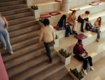 University students on campus, walking around and sitting on large stairs.