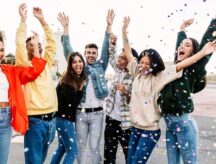Group of friends celebrating with confetti, outside, jumping for joy.