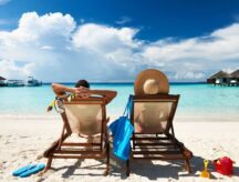 A couple at the beach in the Maldives, laying on two lounging chairs with their backs to the camera.