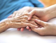 A caregiver comforts an elderly woman, close-up on hands.