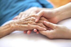 A caregiver comforts an elderly woman, close-up on hands.