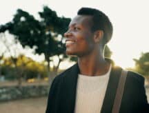 Upper body shot of a man in a white shirt and black blazer smiling as he walks outside.