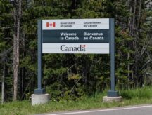 A sign that says "Welcome to Canada" on the side of a road, with greenery surrounding it.