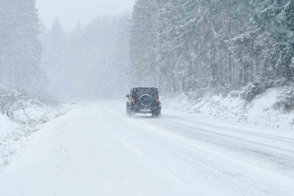 A jeep driving through a snowstorm in the country, with low visibility due to snowfall.