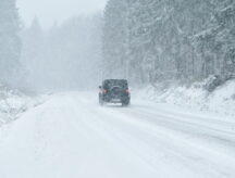 A jeep driving through a snowstorm in the country, with low visibility due to snowfall.