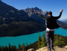 Man stands on a cliff, overlooking Peyto Lake in Alberta, Canada, with mountains visible all around.