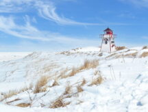 Red and white lighthouse located in the National Park at Covehead, PEI, Canada—surrounding area covered in snow.
