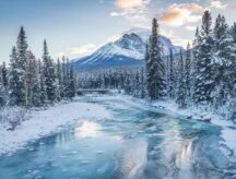 A shot of a frozen river, snow-capped mountains, and coniferous trees taken in Banff, Alberta.