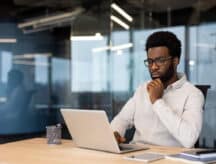 Man in business clothing, in a work office, staring thoughtfully at the laptop before him.