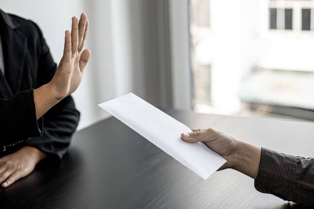 One person declining a white envelope being handed to them by another person—only hands visible.