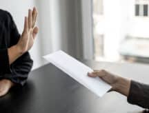 One person declining a white envelope being handed to them by another person—only hands visible.