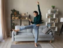 Woman with long curly hair expressing joy by jumping/dancing in her living room.