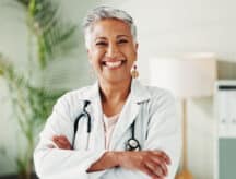 Female doctor with short grey hair smiling at the camera with her arms crossed.