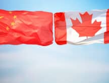 The national flag of China and Canada together against a blue sky.
