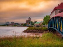 A shot of the Petitcodiac river in Moncton, New Brunswick, with buildings and a pedestrian bridge visible.