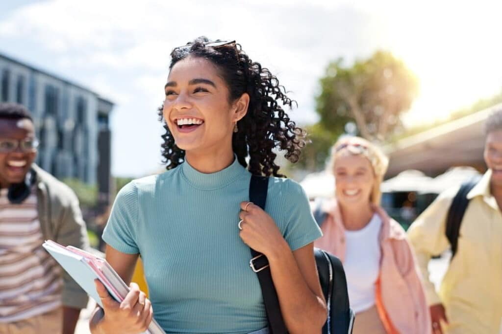 Happy female student with a backpack over one shoulder laughing with her friends.