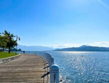 A shot of a boardwalk in Kelowna, BC, on a clear sunny day with Okanagan Lake and mountains visible in the background.