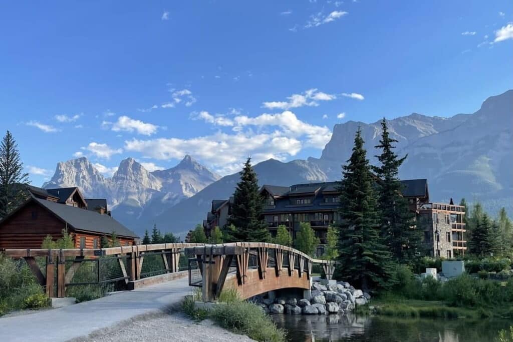 A wooden bridge over Spring Creek, Canmore, Alberta, with the Three Sisters peaks in the Canadian Rockies in the background.