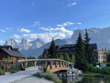 A wooden bridge over Spring Creek, Canmore, Alberta, with the Three Sisters peaks in the Canadian Rockies in the background.