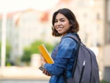 Smiling female student with a backpack and a notebook in her hands, turning toward the camera.