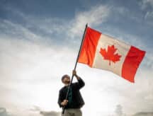 Man happily waving a very large Canadian flag against a semi-cloudy sky.