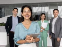 A business woman looks into the camera, with other managers in the background