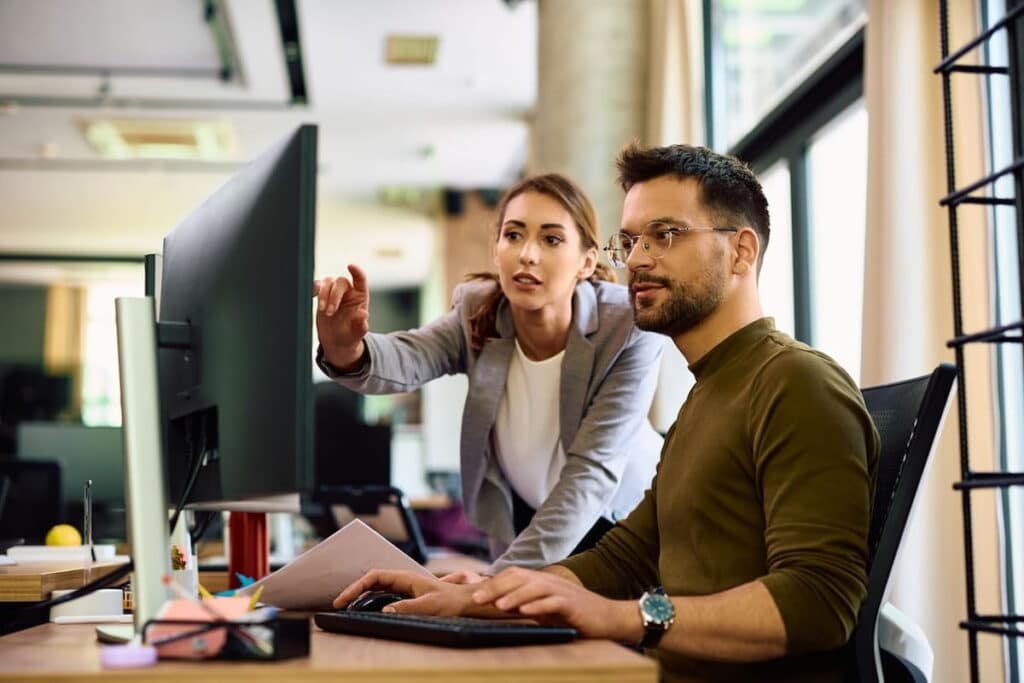 Man and woman looking at a desktop together in an office space.