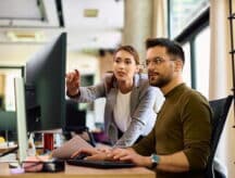 Man and woman looking at a desktop together in an office space.