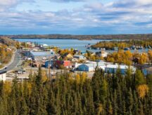 A shot of Yellowknife, showing buildings, greenery, and surrounding lake.