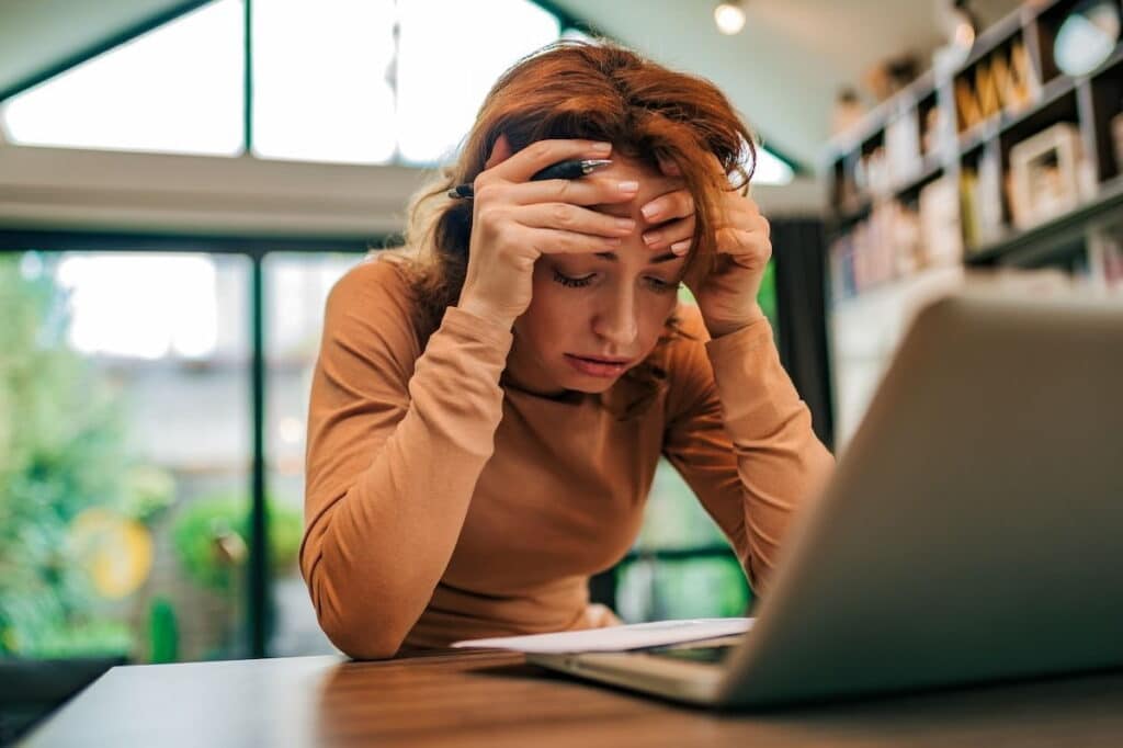 Dejected woman sitting at a table, holding her hands in her head.